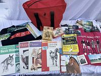 Overview photo of all lot items including sweatshirts, bag, books, ornaments, and photographs on white cloth background