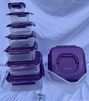 Eight clear rectangular containers stacked on left side, largest container and lid on right side. Purple lids with locking tabs and handle on largest container lid visible.