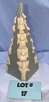 Front view of the triangular pyramid shaped Noscone statue with multiple carved faces and 1986 mark at base.