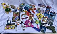 Full view of assorted kids toys and novelty items on white background including plush toys, markers, clappers, stickers, and kites.