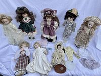 Ten vintage dolls displayed on white backdrop, most standing on individual stands, with extra clothes laid out in front