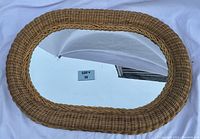 Oval wicker framed mirror laid flat, showing reflective mirror surface with some spots visible.