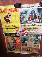 Full view of four vintage movie posters and two movie magazines on wooden floor.