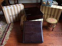 Four Bombay-branded container boxes of different sizes and styles on a wooden floor with striped Bombay packaging boxes behind them