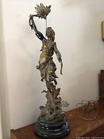 Full view of the lamp sculpture showing the entire female figure standing on base with leaf motifs, light fixture on raised arm and pull chain.