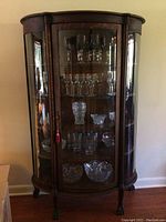Full front view of curved glass-front wooden curio cabinet with contents inside.