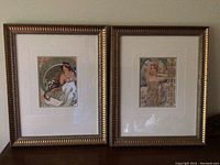 Two framed art prints leaning on wall with white matting and gold-tone beaded frames, showing visible scratches on frames.