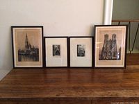 Four framed architectural prints placed side by side on a wooden table against a neutral wall