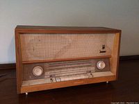 Full front view showing wood cabinet, woven fabric speaker grille, and front control panel with knobs and push buttons.