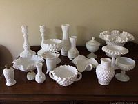 Full view of milk glass collection with various bowls, candlesticks, vases, and decorative items spread on wooden surface.