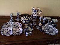 Full view of the entire collection arranged on a wooden surface, showing candlesticks, pitcher, divided tray, small bowls, lidded container, and other small ceramics mostly in blue and white floral designs.