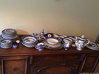 Wide view of assorted plates, bowls, platters, teapot, sugar bowl, creamer and cups arranged on sideboard