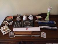 Full view of all miscellaneous decorative items arranged on a wooden surface including porcelain pieces, cutlery boxes, and a glass vase