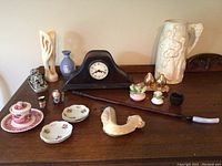 Overview of all decorative items on wooden surface including ceramic, porcelain items, and carved pipe.