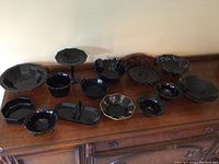 Wide view of the assortment of black glassware on wooden surface showing various items in lot with different shapes and sizes.