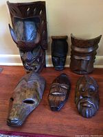 Full set of six miscellaneous wooden carved masks arranged on a wooden surface