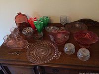 Full view of glassware collection on wooden surface including handkerchief vases, clear glasses, bowls, and plates.