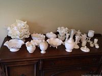 Full view of all milk glass pieces arranged on wooden chest displaying various sizes and shapes.