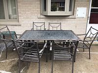 Full view of patio table with six matching chairs arranged around it, showing glass tabletop and metal frames