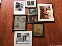 Eight framed photographs and drawings arranged on a wooden floor, showing a mix of portraits and candid images with various framing styles