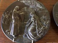 Close-up of a single Merri Roderick decorative plate depicting a seated figure being approached by a standing figure with other figures and a textured background.