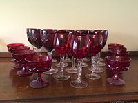 Full set of red glass goblets and compote glasses on wood surface, various styles and sizes.