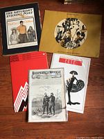 Full view of vintage posters and prints on wooden floor, showing collection including The Saturday Evening Post, Erte print, Harper's Weekly cover, and others