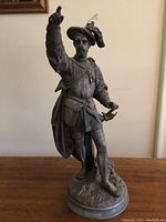 Full view of the bronze statue depicting a man in Renaissance clothing with one arm raised.