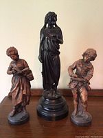 Three wood statues shown together on wood furniture, with central taller female figure and two smaller figures on either side.