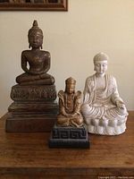 Front view of three Buddha statues including large dark bronze, small bronze, and white statue on lotus base.