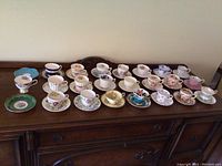 Front view of all 20 teacup and saucer sets on wooden sideboard