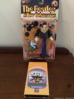 Front view of unopened The Beatles Yellow Submarine figurine in blister packaging, showing a male character and a small blue-faced character figure, with the title branding visible on the card backing.