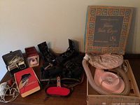 Overview photo showing various vintage grooming appliances including boxed General Electric hair dryer, electric clippers, and grooming accessories on a table.