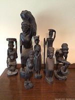 Photo of eight carved wooden human figurines placed on a wooden surface, showcasing various poses and details of the carvings.