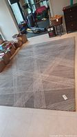 Full view of grey area rug laid on tiled floor with boxes and vacuum in background