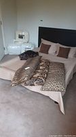 Queen size bed with beige comforter, brown pillows, and three animal print body pillows laid on bed