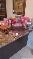 Front angle view showing the collection of board games arranged on countertop including Scrabble, Labyrinth, Risk, Clementoni City Quiz, and others with a dice tray and game pieces.