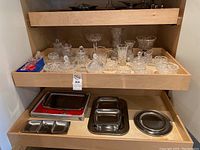 Full view of wooden shelf with upper drawer holding crystal items including vases, bowls, jars, and the lower shelf holding various metal serving trays and dishes