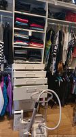 Closet shelving with folded pants, hanging scarves and a steamer unit on floor