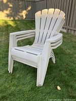 Three white plastic Adirondack chairs stacked together showing overall condition and design.