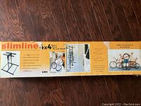 Box featuring product name, brand Slimline 4x4 Space Saver Bicycle Stand, showing bikes stored vertically with helmets on top, demonstrating storage of 4 bikes and 4 helmets.