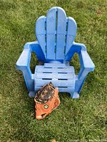 Front view of toddler blue plastic Adirondack chair with Wilson baseball glove placed on seat in grass.