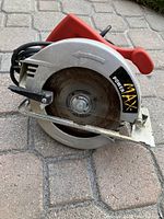 Side view of the Powermax circular saw showing the metallic blade guard with the brand sticker and red handle with attached cord.