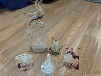 Photo showing all six crystal figurines placed on floor, including tall peacock, Scottish bagpipe player, antique phone, teapot, and two smaller decorative pieces