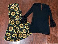 Two dresses laid flat on wood floor, one black sleeveless with sunflower print, the other black long sleeve with feathered cuffs