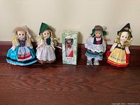 Wide view of five European dolls including boxed Heidi doll and four other dolls in traditional costumes standing upright on wooden floor against wall