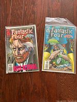 Two Fantastic Four comic books on wood floor, sleeved with backer boards, showing front covers distinctly.