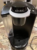 Front and top view of the black Keurig coffee maker showing the water reservoir, drip tray, and control panel.