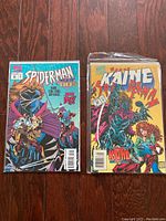 Two vintage Marvel comic books featuring Spider-Man and Kaine in protective sleeves with backer-board on wooden floor