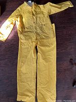 Full front view of the yellow rain pants with suspenders laid flat on wooden floor, showing condition and design